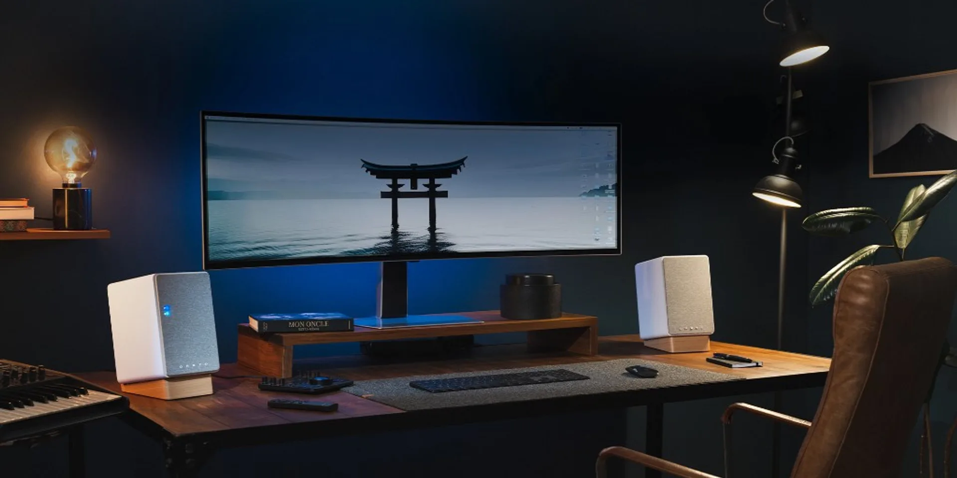 Dark home office with ultrawide curved monitor and white bookshelf-style powered monitors on wooden wedge stands, warm accen…