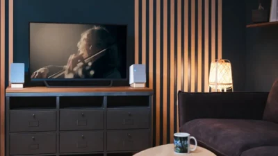 Onkyo Creator compact grey fabric speakers with wood bases on a dark media console flanking a TV in a teal and wood-slat liv…