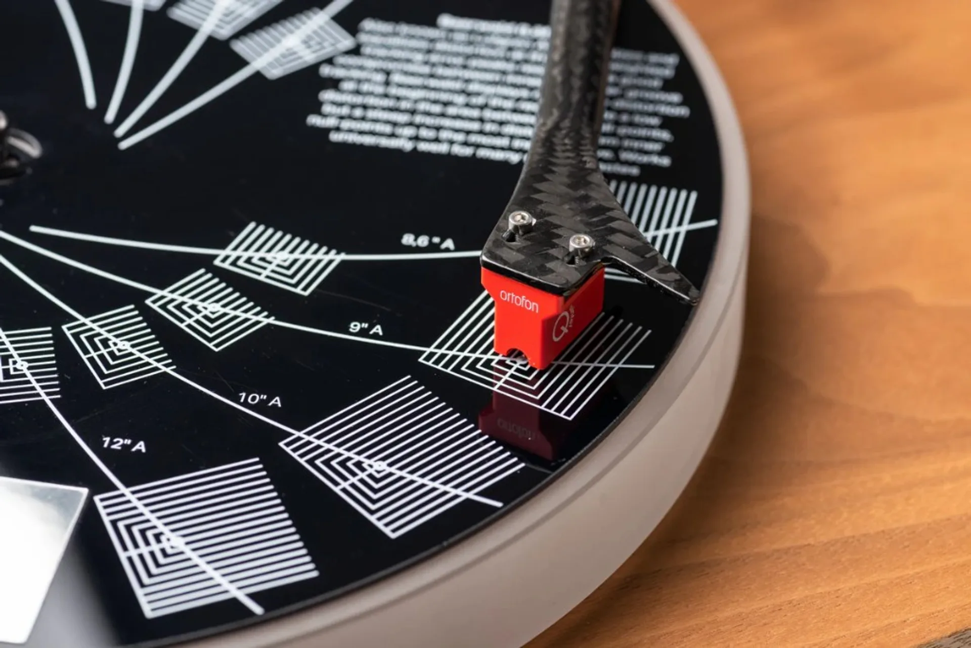 Red Ortofon cartridge on carbon fiber headshell, stylus on black alignment protractor atop a turntable platter.