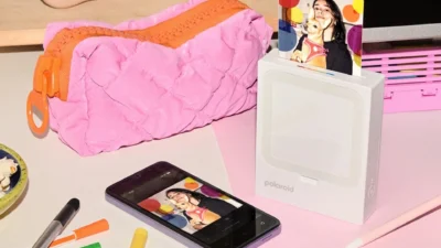 Polaroid Hi-Print 3x3 lifestyle scene with printed photo, smartphone app preview, and desk stationery.