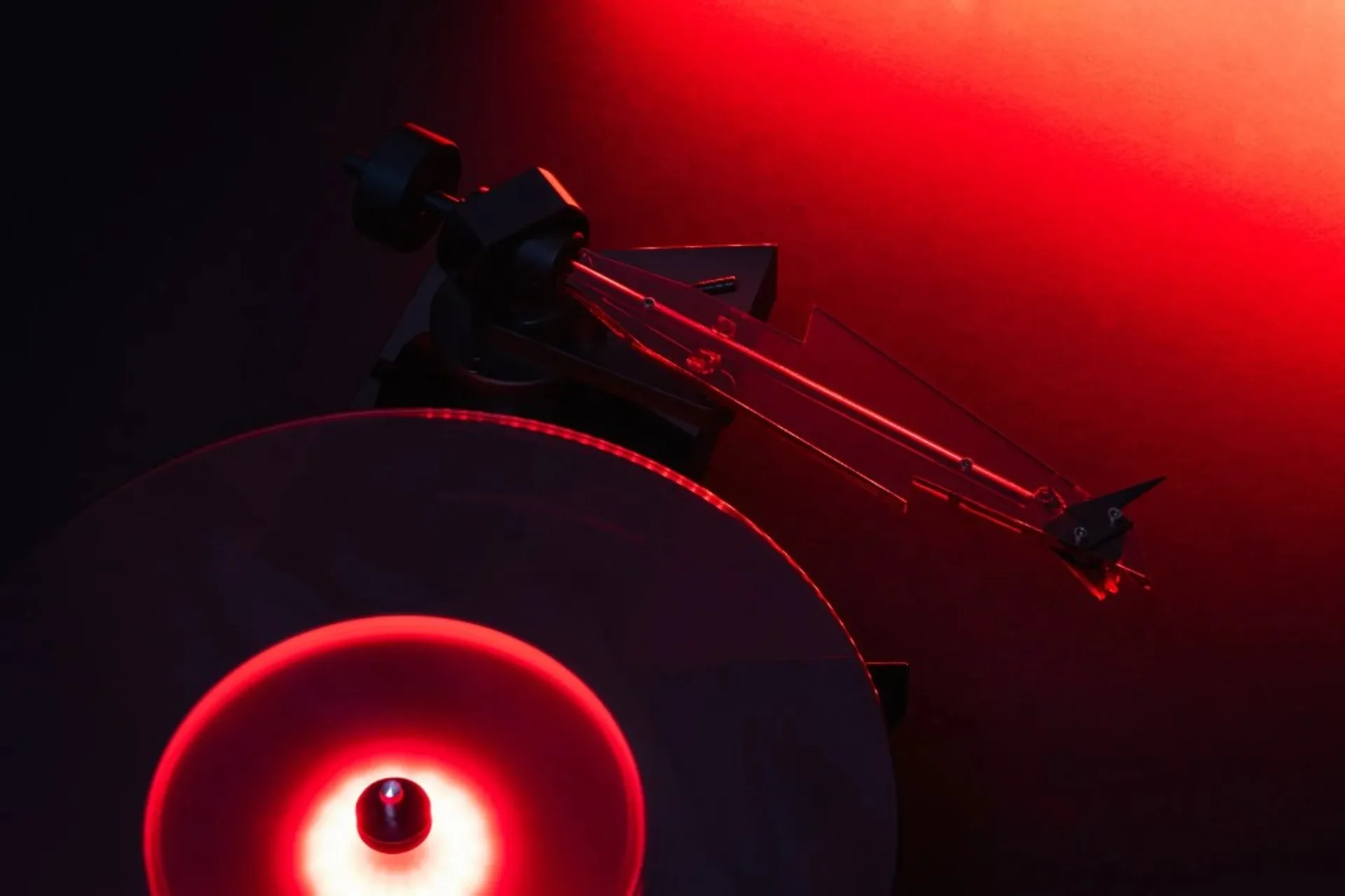Pro-Ject AC/DC limited edition turntable: clear acrylic lightning-bolt tonearm and red-lit platter in dramatic red lighting.
