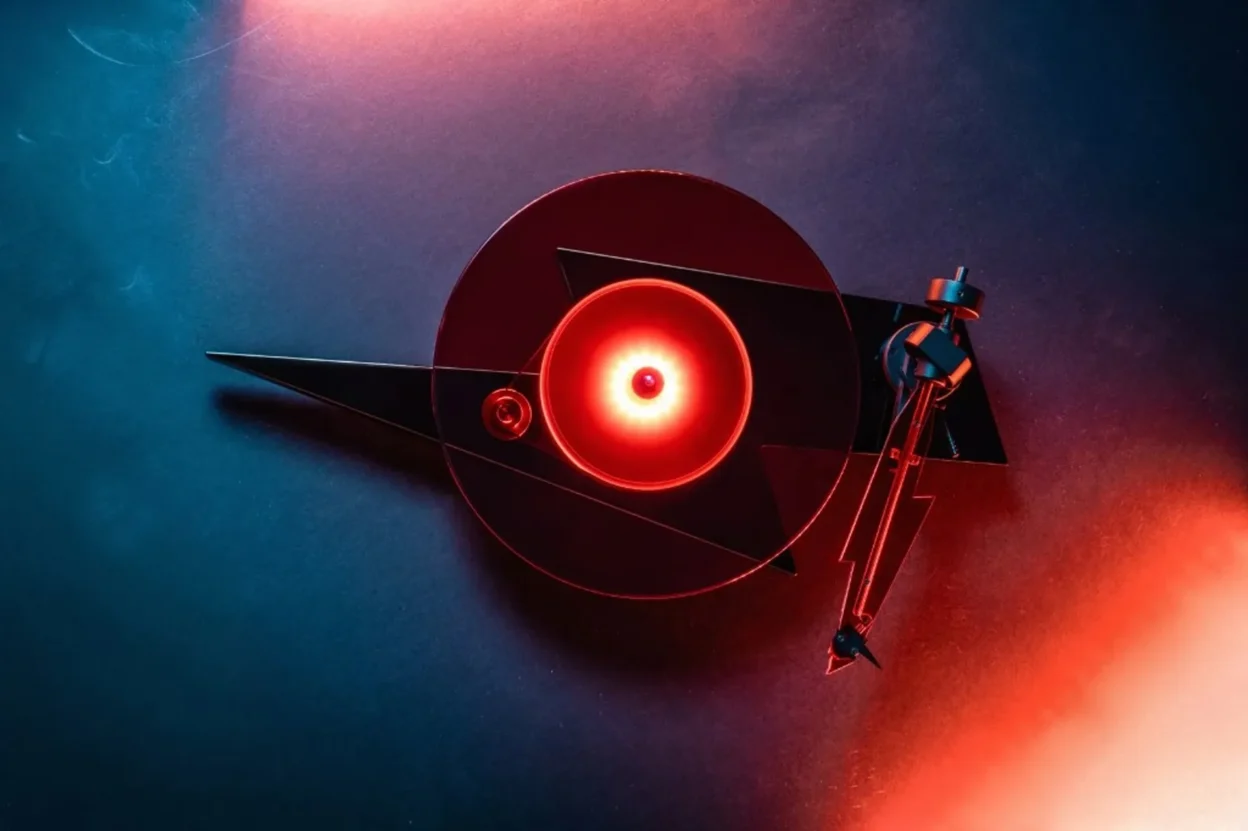 Top-down view of Pro-Ject AC/DC limited edition turntable: lightning-bolt plinth and glowing red glass platter under blue an…