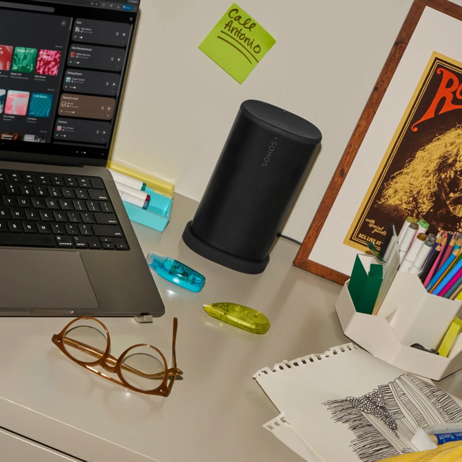 Sonos Play black speaker on a desk near a laptop in a home office scene with notebooks and stationery.