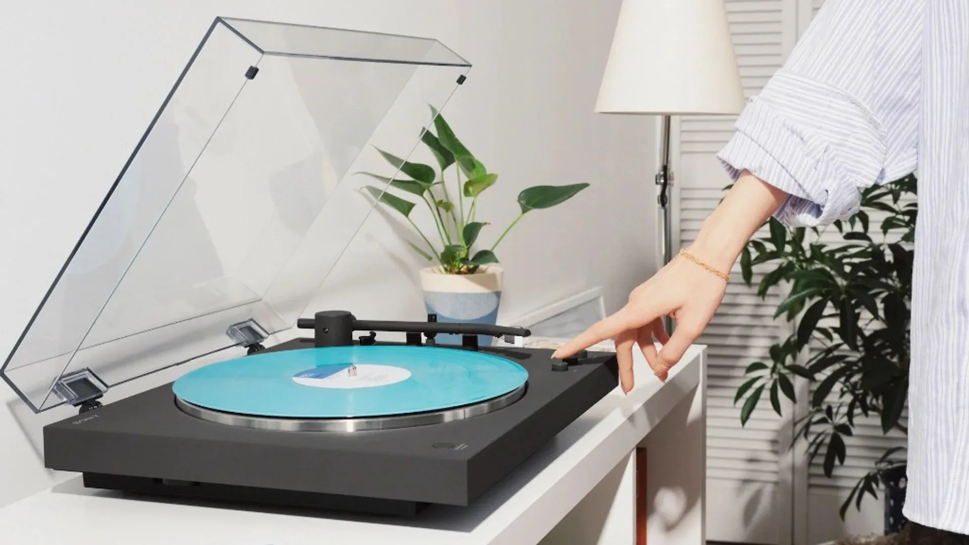 Black Sony turntable with turquoise vinyl in a bright modern room, hand on front control