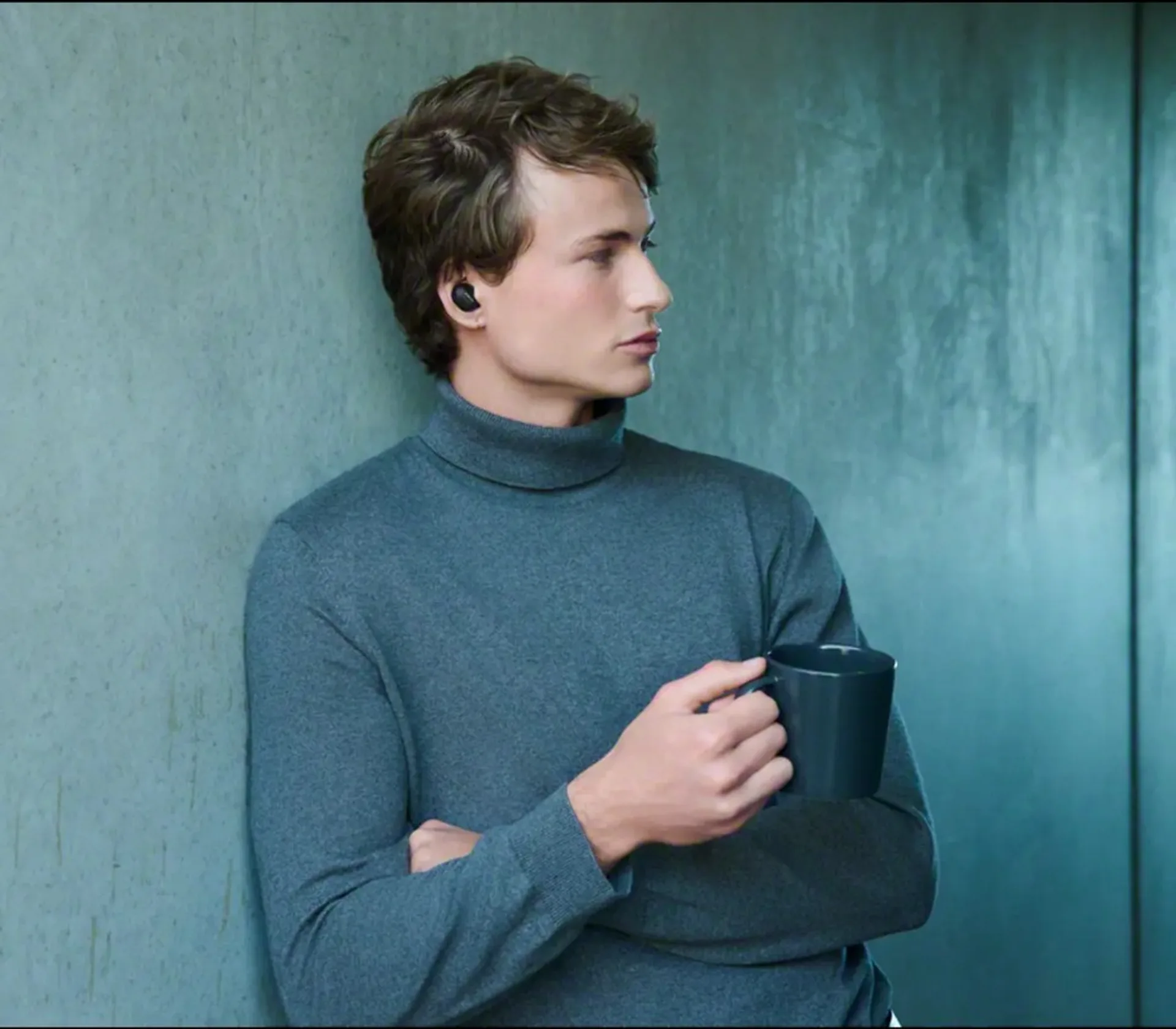 Person wearing Sony WF-1000XM6 earbuds holding a mug indoors, lifestyle portrait.