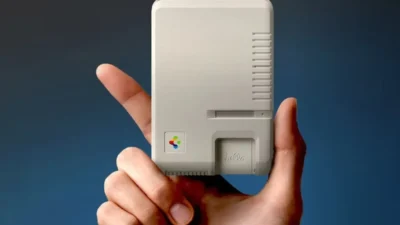 Hand holding a small beige Spigen accessory styled like a classic Macintosh with hello script and retro vents.