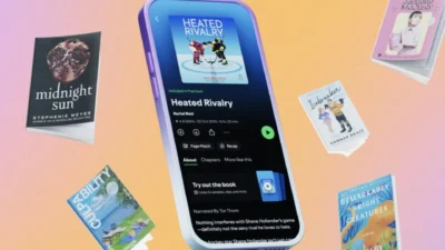Spotify app on a phone showing audiobook Heated Rivalry, with floating bestseller covers on a pastel gradient.