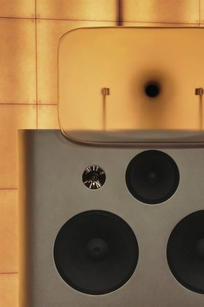 Close-up of Friendly Pressure speaker drivers and amber translucent horn against warm square acoustic panels.
