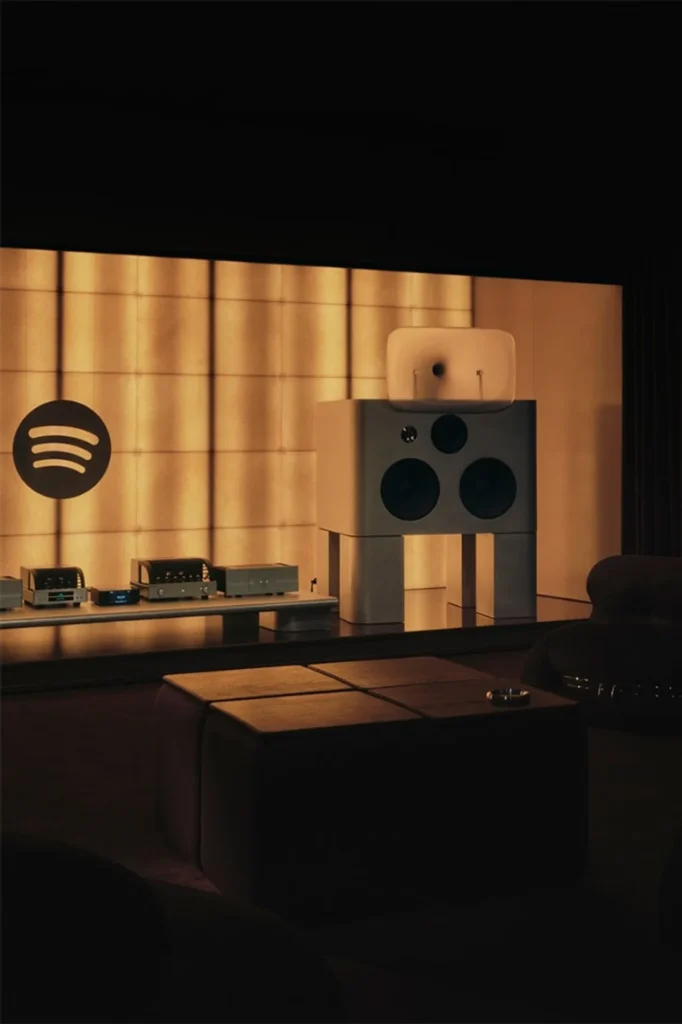 Spotify Listening Lounge with large white speakers, glowing grid wall, tube gear on low platform, and dark lounge seating.
