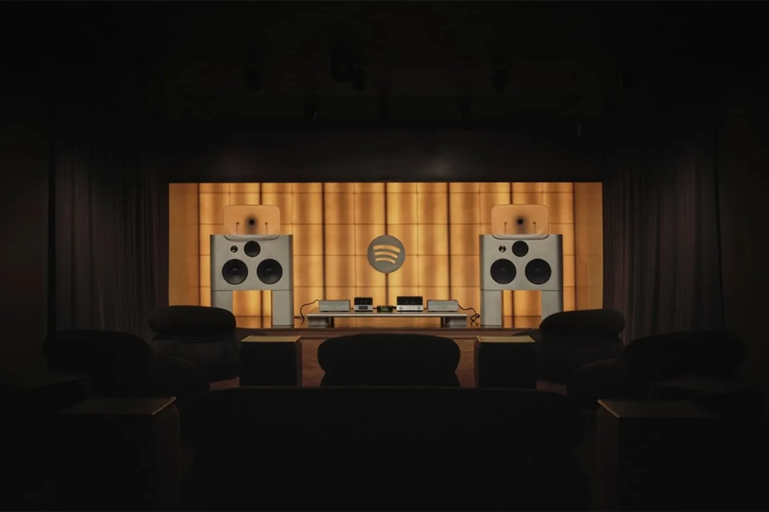 Wide shot of Spotify Listening Lounge stage with twin large speakers, Spotify logo on golden backlit wall, and audience seat…