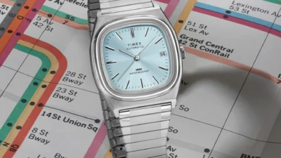 Timex Automatic 1983 E Line with ice blue dial and date at three o'clock, stainless expansion bracelet on a colorful metro map.