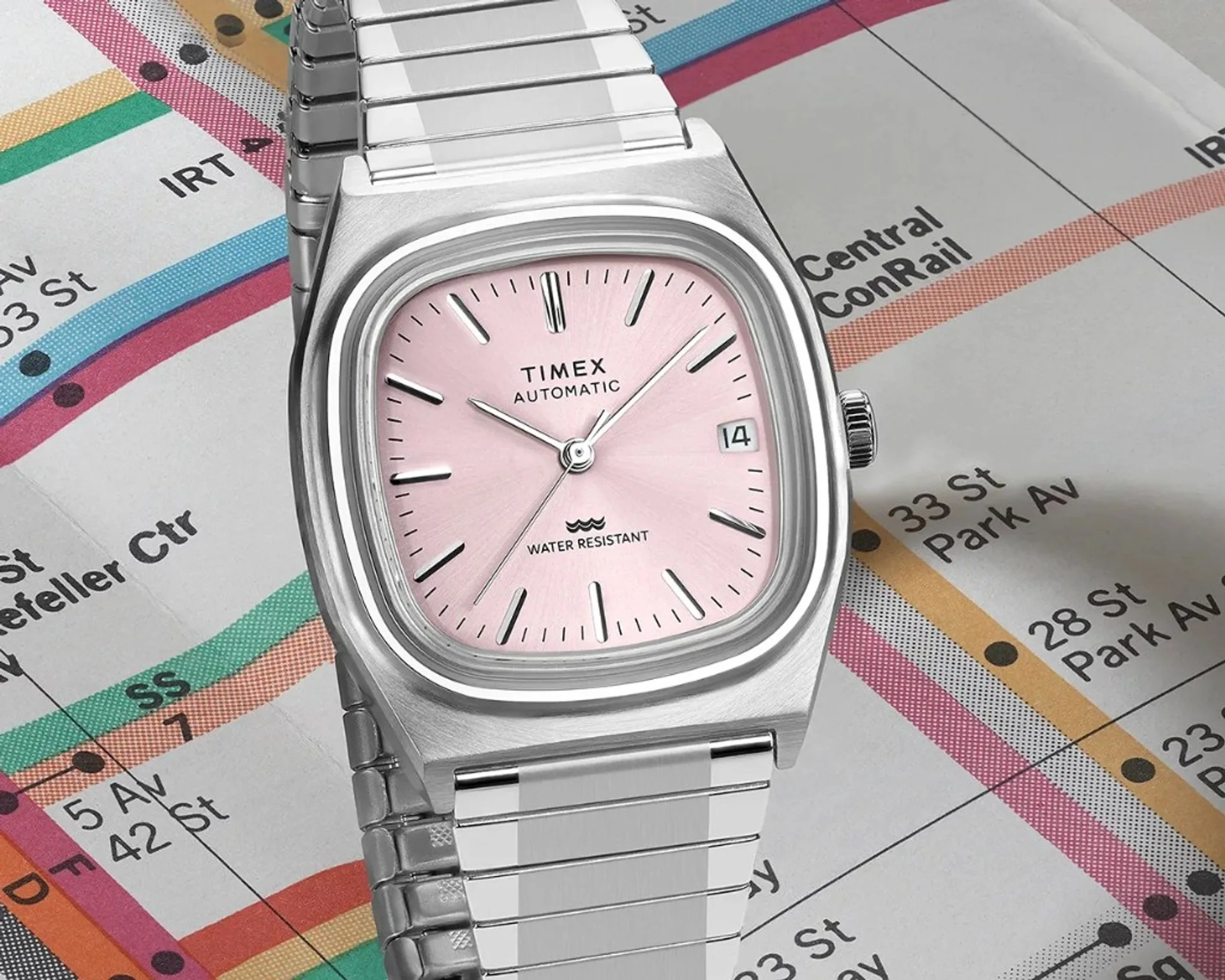 Timex Automatic 1983 E Line watch with light pink sunray dial, stainless steel cushion case and expansion bracelet, on a vintage-style subway map.
