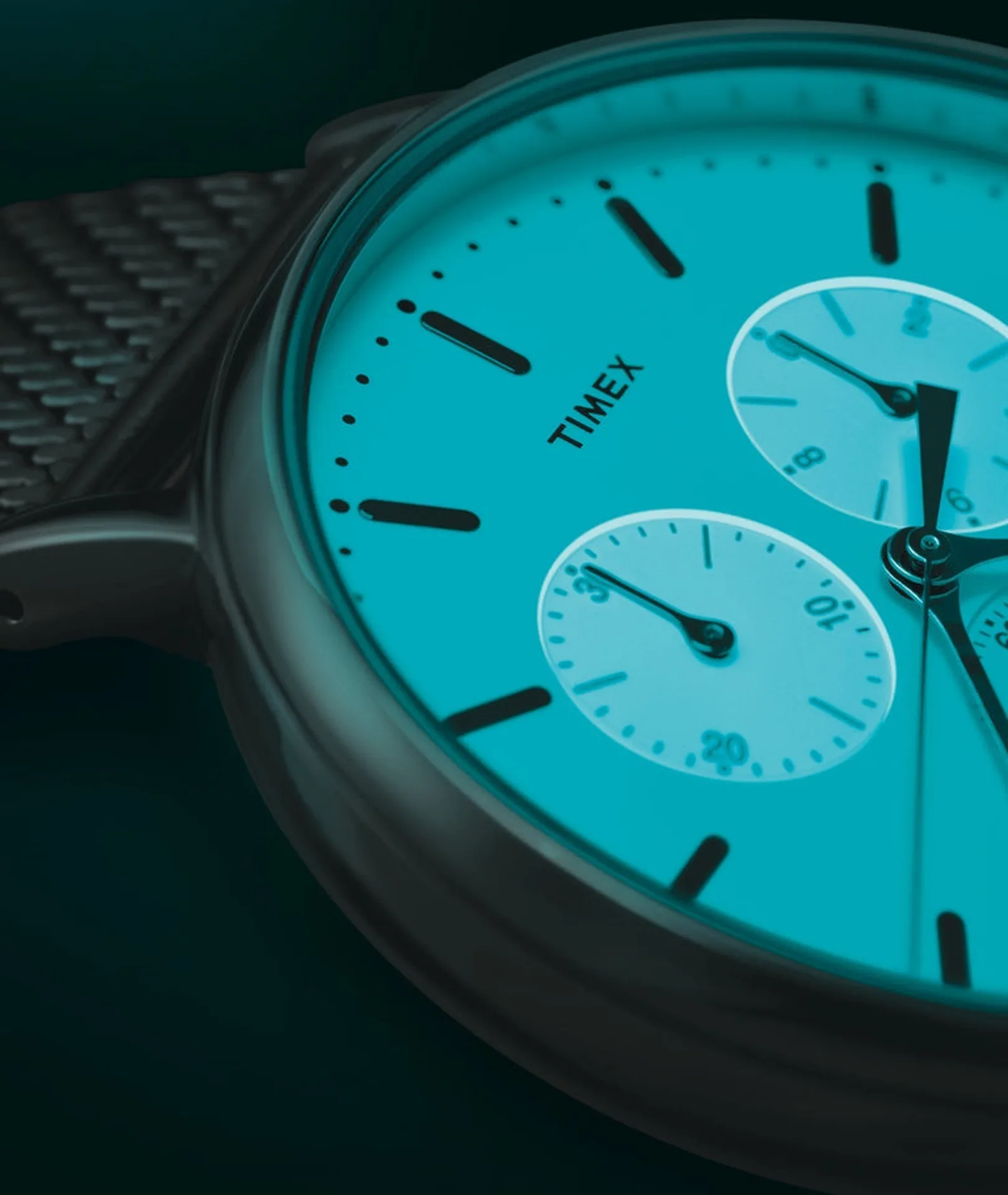 Close-up of a modern Timex chronograph with glowing teal dial, black baton indices, white sub-dials, TIMEX logo and black Mi…