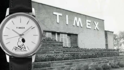 Composite: modern Timex analog watch with Snoopy on dial and black leather strap over black-and-white photo of Timex buildin…