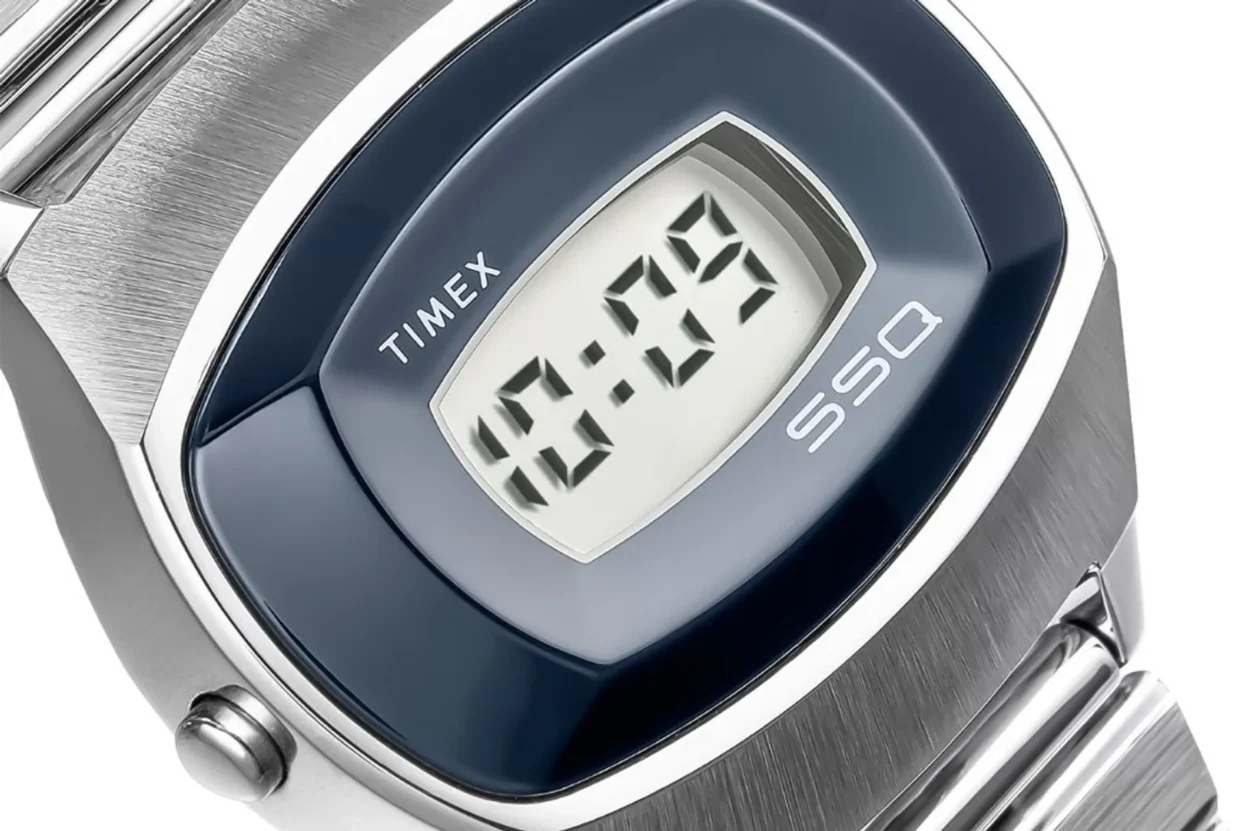 Close-up of Timex SSQ digital watch: rectangular LCD at 10:09, glossy blue cushion bezel, brushed stainless case and bracele…
