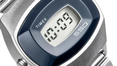 Close-up of Timex SSQ digital watch: rectangular LCD at 10:09, glossy blue cushion bezel, brushed stainless case and bracele…