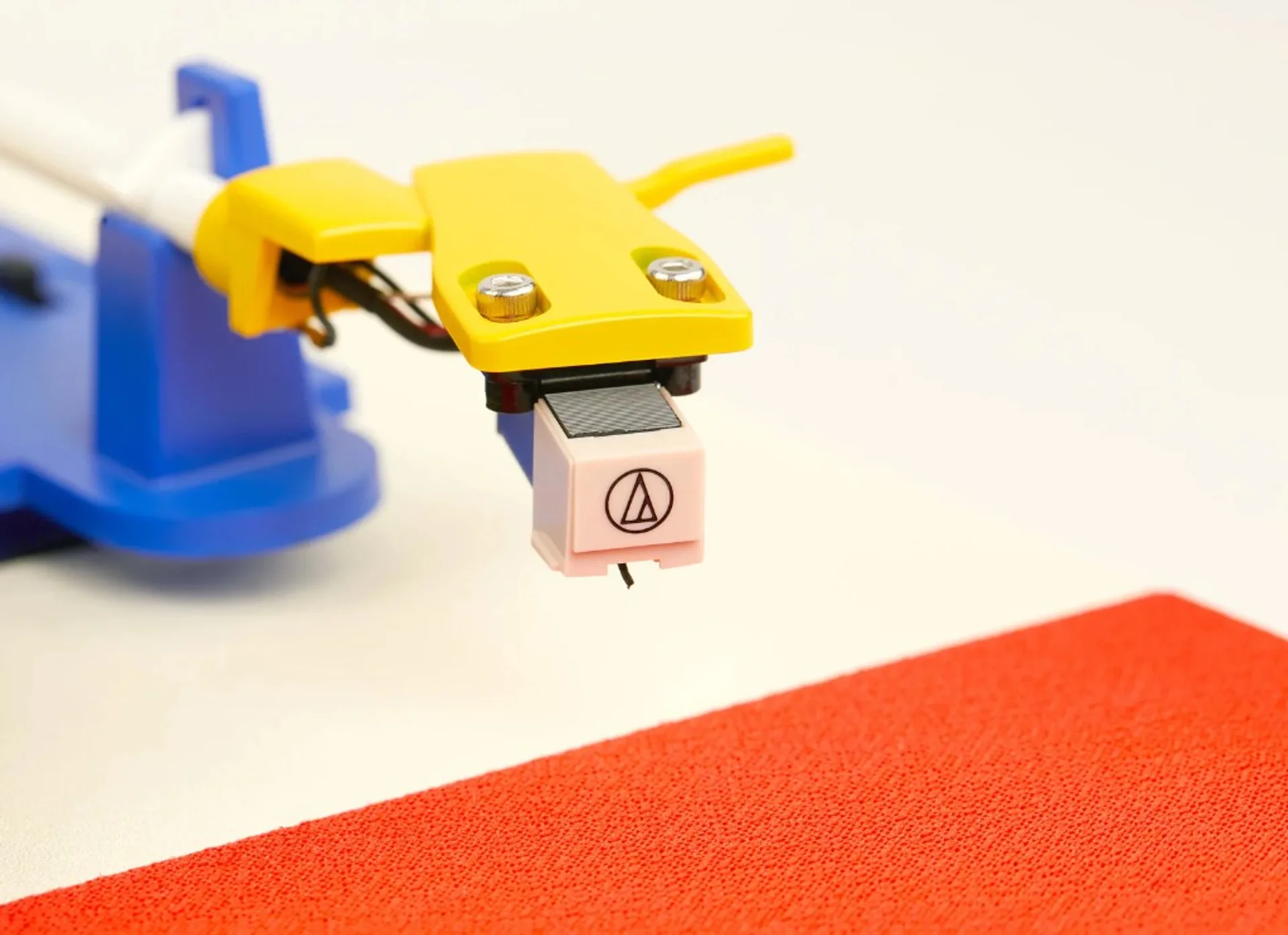 Close-up of Tinyl Play Pro yellow headshell and light pink Audio-Technica phono cartridge with stylus, blue arm rest, and re…