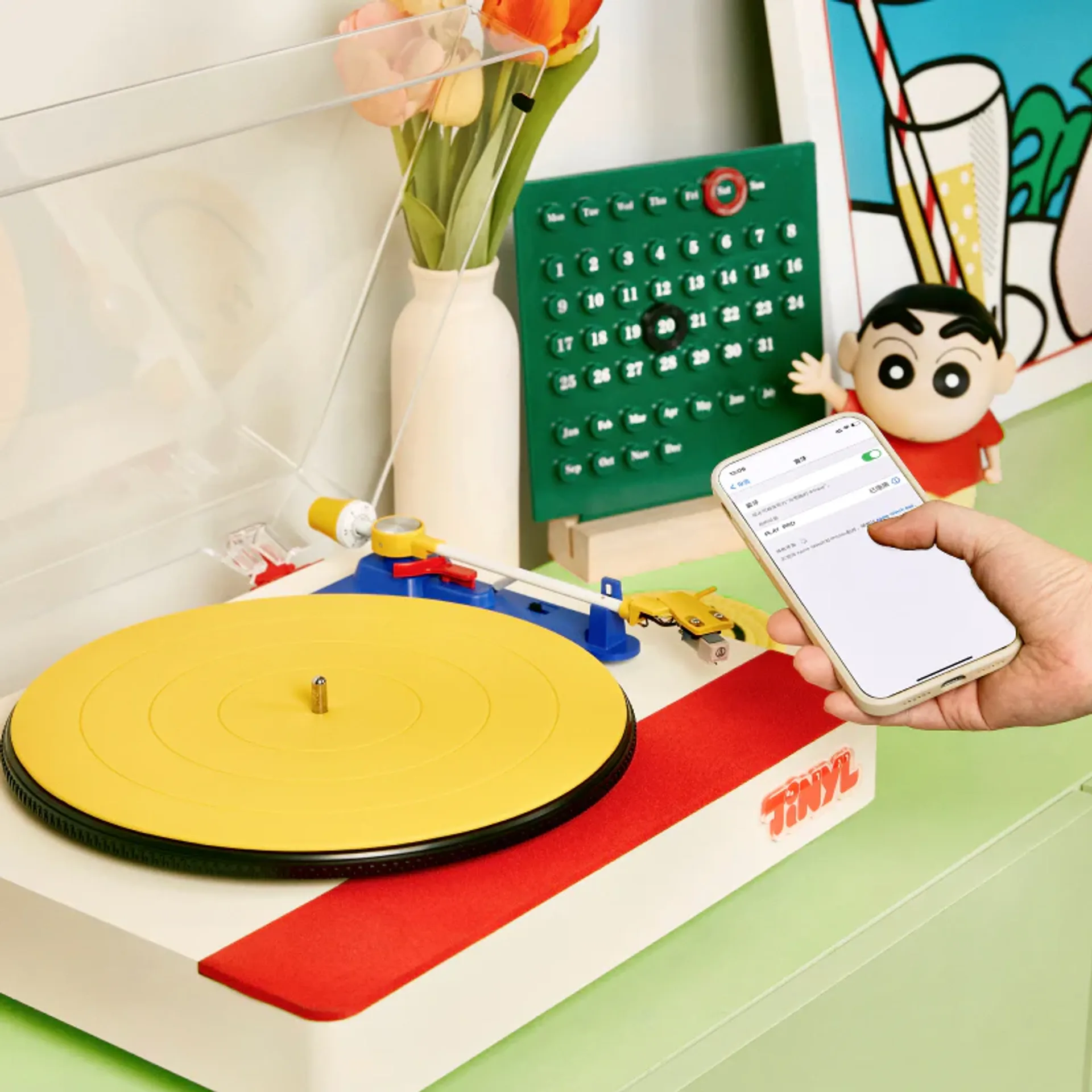 Tinyl Play Pro colorful turntable on a green surface with a smartphone showing Bluetooth connected to PLAY PRO in a bright p…
