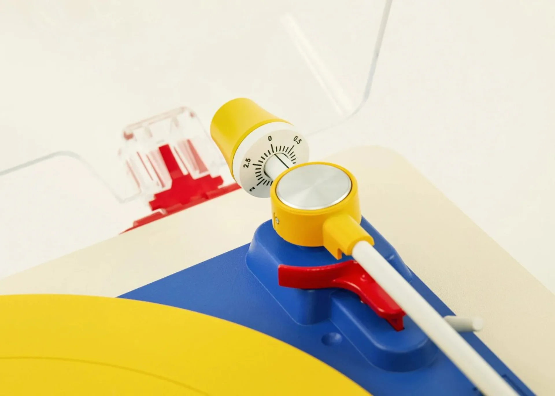 Macro detail of Tinyl Play Pro tonearm: yellow counterweight dial, white arm, red cue lever, and blue pivot housing on a yel…