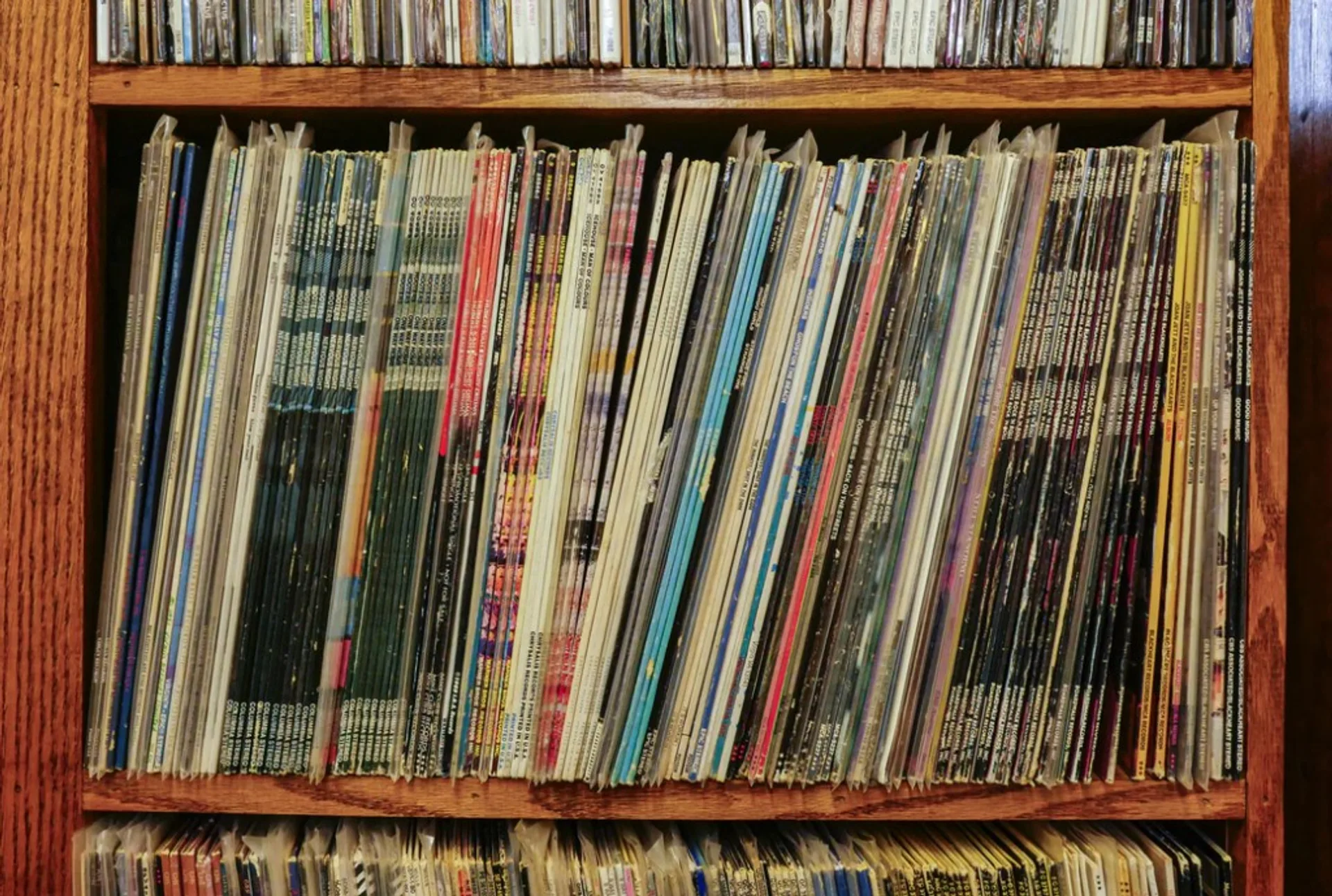 Wooden bookshelf packed with vinyl LPs in sleeves, colorful album spines