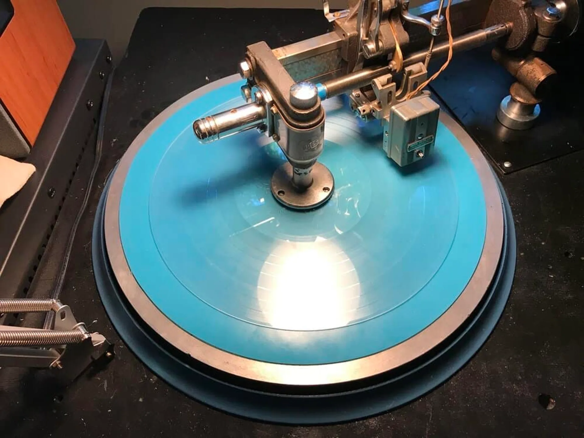 Vinyl mastering lathe with bright blue lacquer disc and precision cutting arm in a professional studio