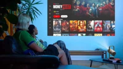 XGIMI Vibe One projecting Netflix on a wall in a dim living room with two people on a sofa watching Money Heist.