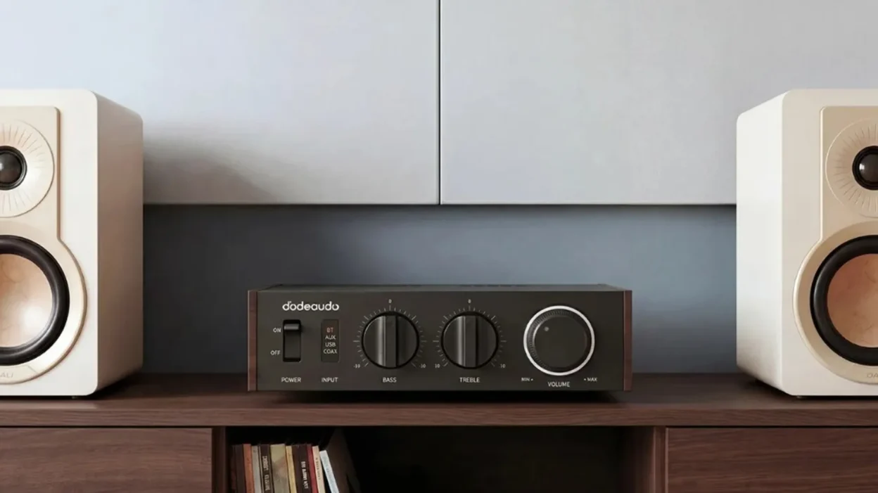 FiiO Jade Audio Level 1 desktop amplifier centered between two white DALI bookshelf speakers on a dark wood shelf.