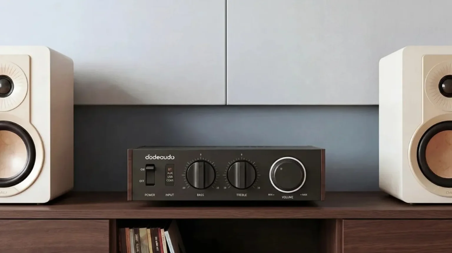 FiiO Jade Audio Level 1 desktop amplifier centered between two white DALI bookshelf speakers on a dark wood shelf.