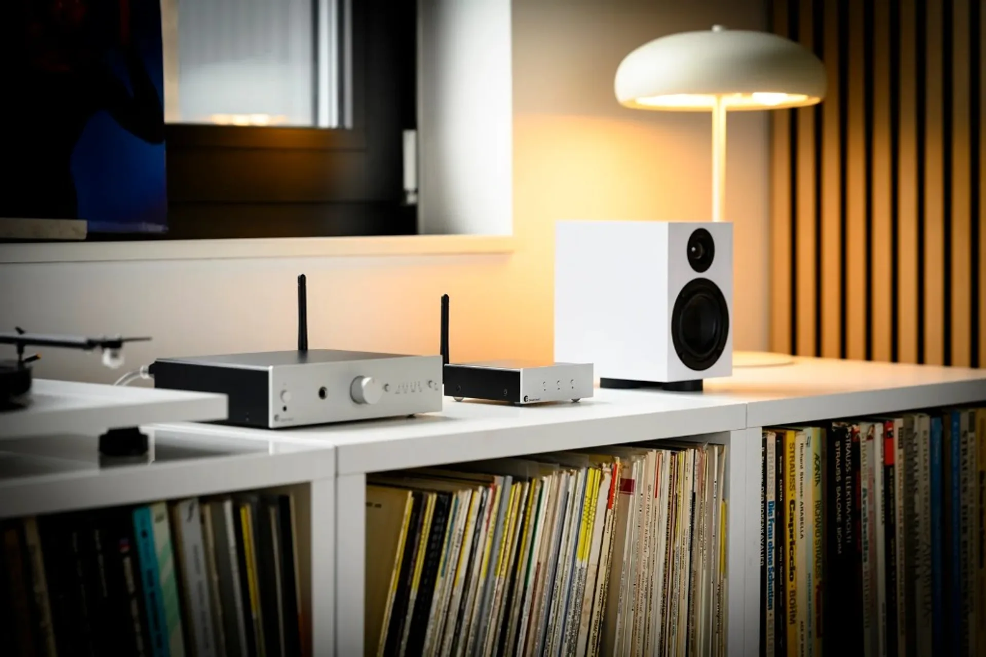 Pro-Ject Stream Box E wireless streamer with silver front panel, control buttons, Wi-Fi antenna, and chrome feet on a white shelf.