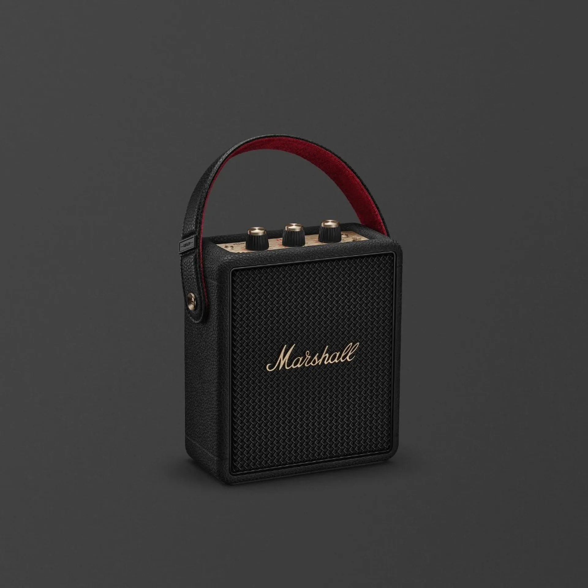 Marshall Stockwell III portable Bluetooth speaker in Black and Brass with gold logo, brass knobs, and red-lined carry strap on dark grey background.