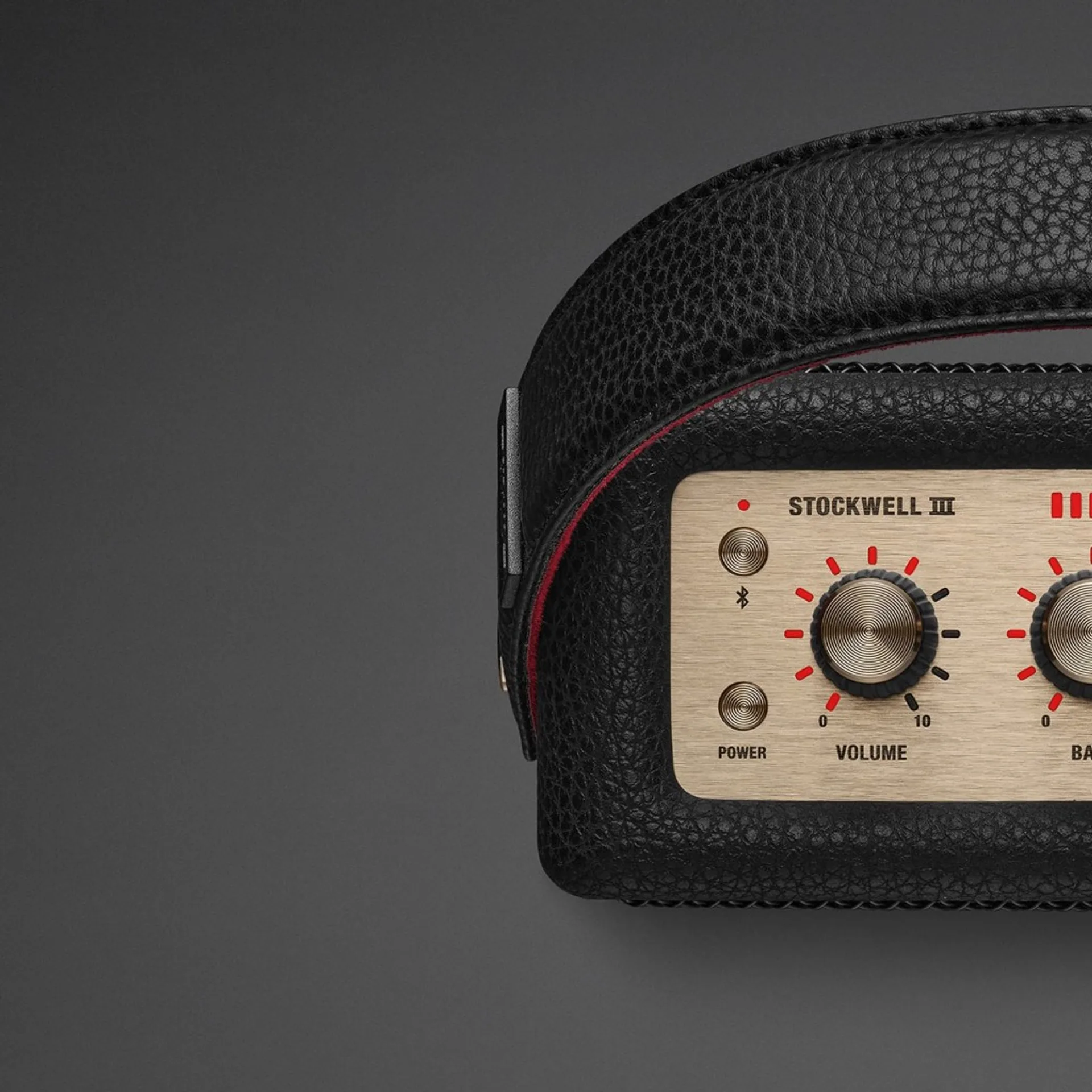 Close-up of Marshall Stockwell III brass top panel with volume, bass, power, and Bluetooth controls and red-lined carry strap.