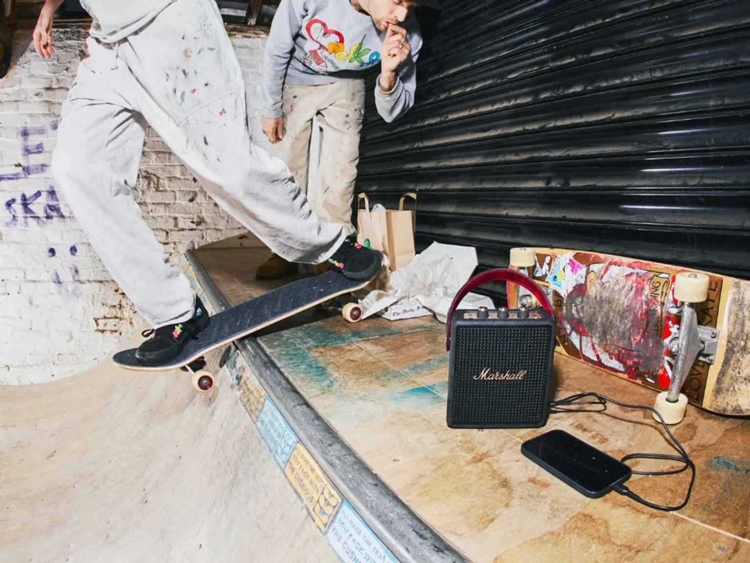 Marshall Stockwell III portable speaker at an indoor skate park connected to a smartphone with skaters in the background.