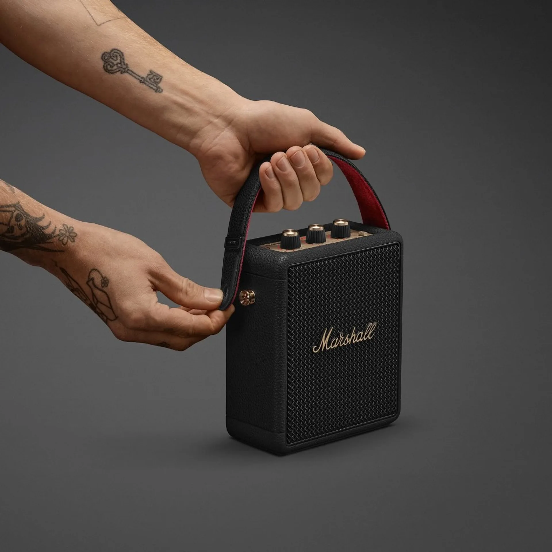 Hands attaching the red-lined PU leather carry strap to a Marshall Stockwell III portable speaker.